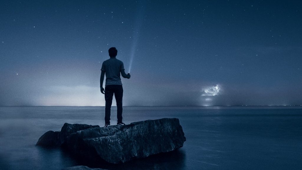 person standing on beach with flashlight