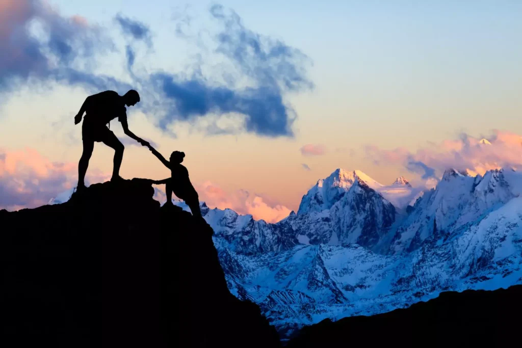 a man helping a woman climb up a mountain, she is trusting him