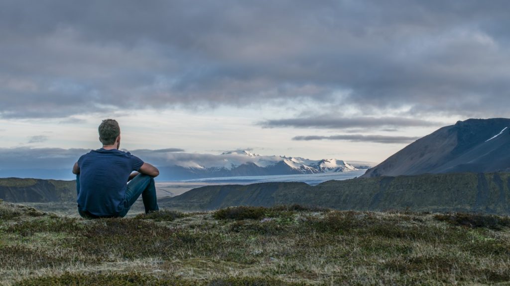 man sitting on mountain overlooking lake