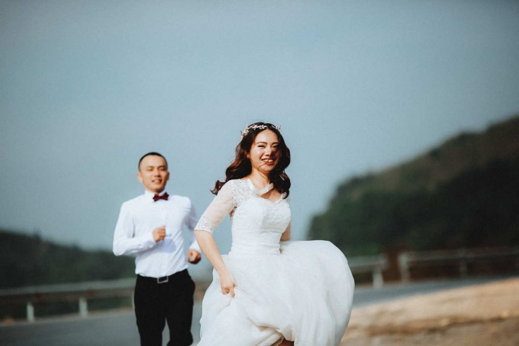 bride and groom running along river