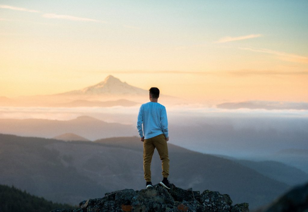 man standing on mountain overlooking mountain range