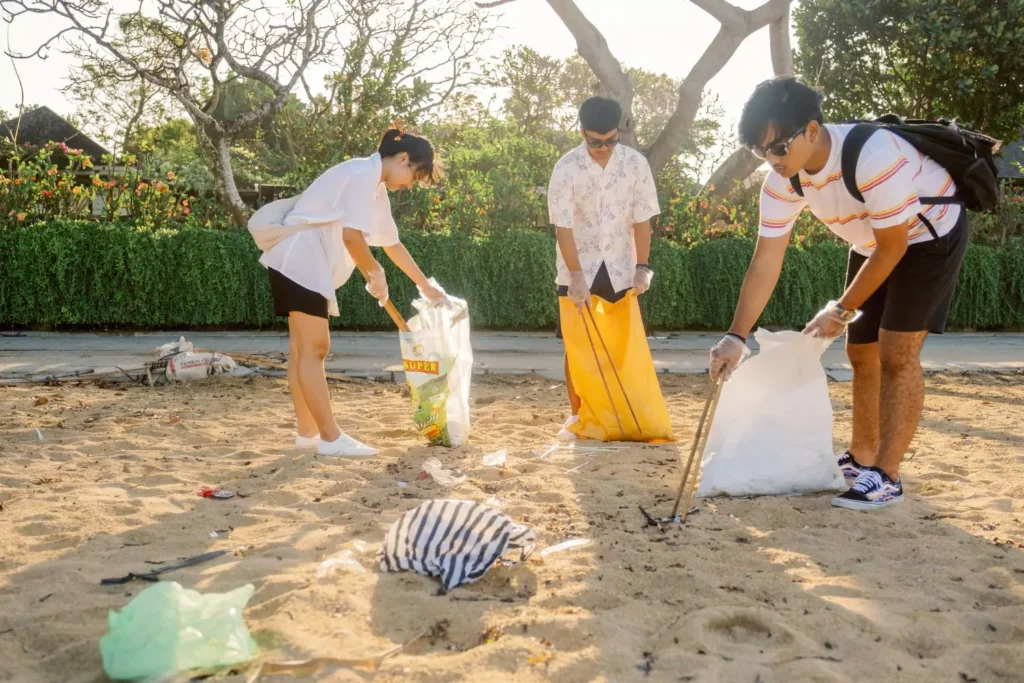 three people pick up trash on a beach, serving the community