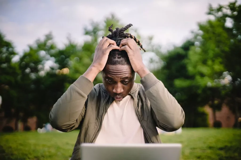 a man looking at his laptop with his hands on his head feeling like a failure