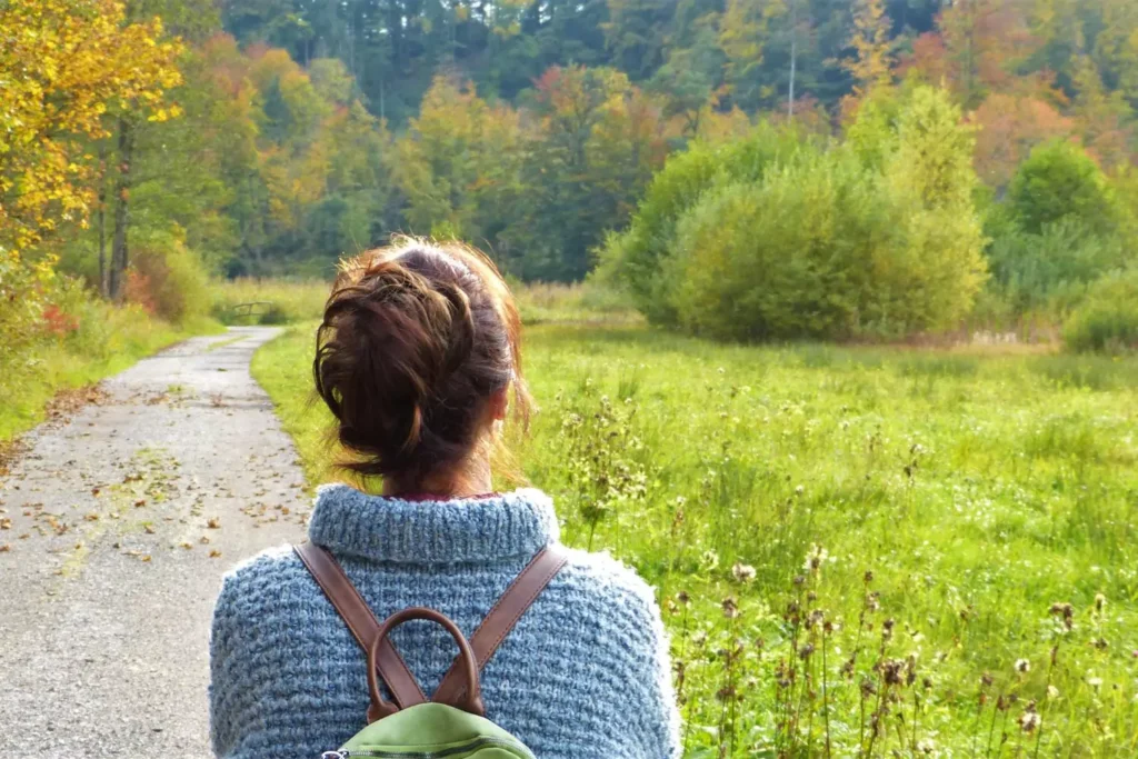 a single woman wearing a backpack looking out over a forrest