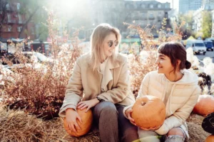 two woman looking at each other holding pumpkins, reflecting