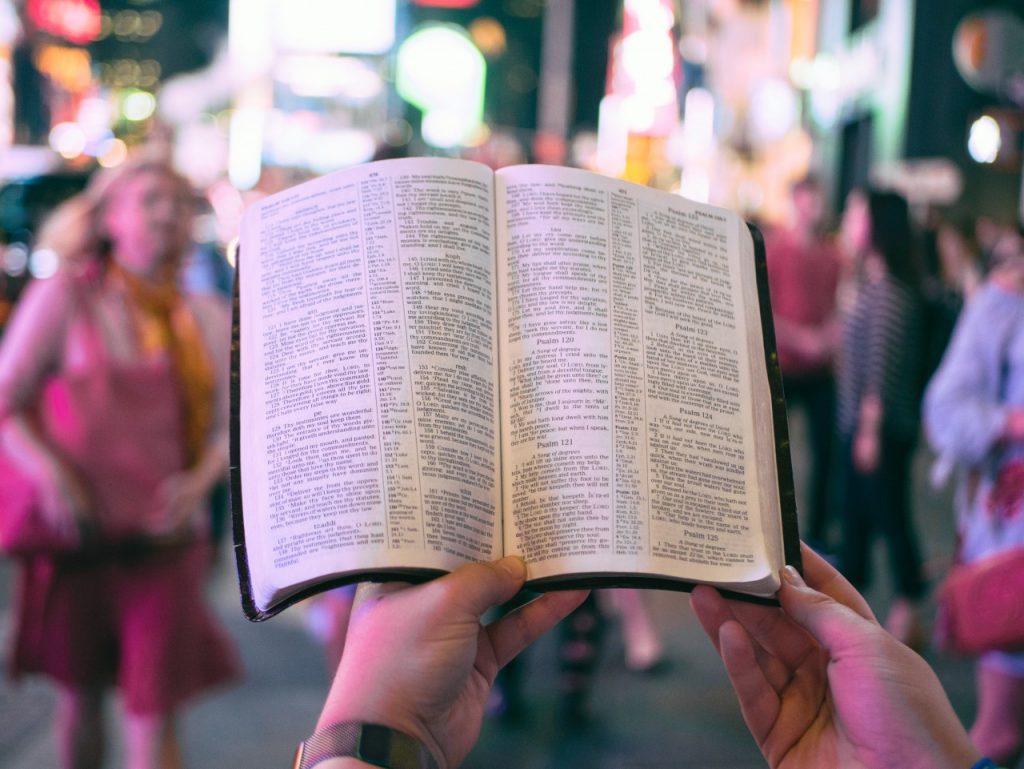 FPV of person holding Bible in front of them in busy city at night