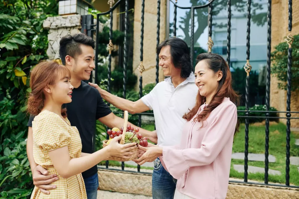 a young man bringing his girlfriend home to meet his parents. She offers a basket of fruit to the mother.