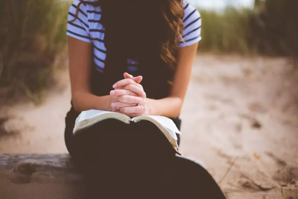 a woman with her hands clasped on her Bible, praying