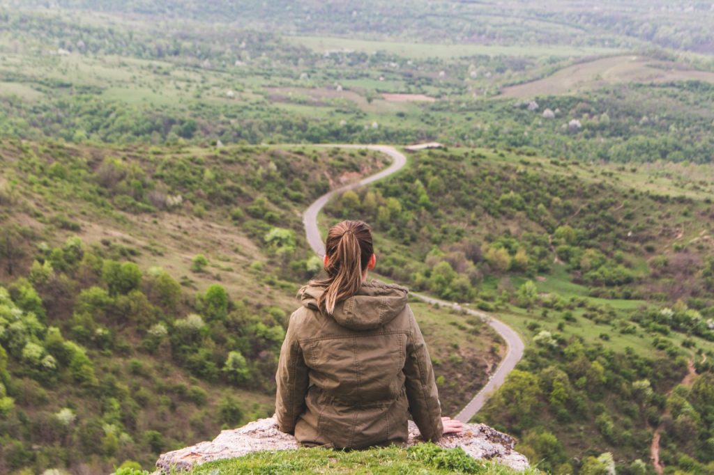 woman sitting on cliff overlooking valley