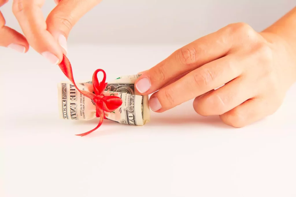 Hands wrapping a dollar in a red bow. Be a cheerful giver.