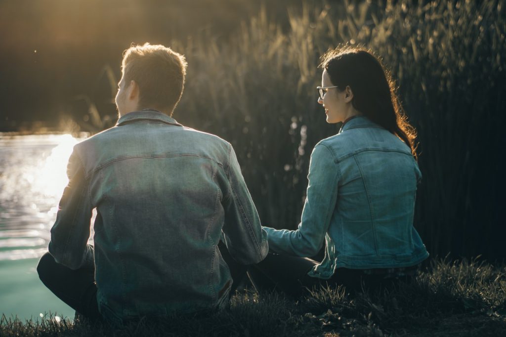 man and woman sitting by lake