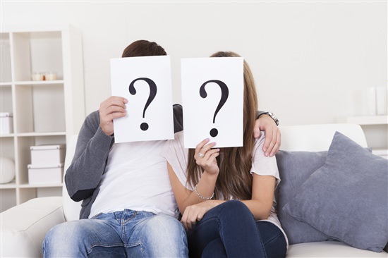 couple sitting on couch holding question marks in front of their faces