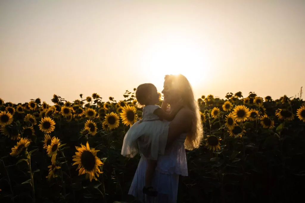 motherhood - a woman holding a toddler amongst sunflowers