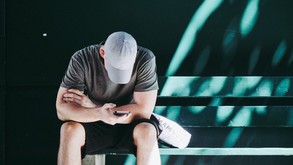 man sitting on bench, with terrible posture, mind you, look at phone