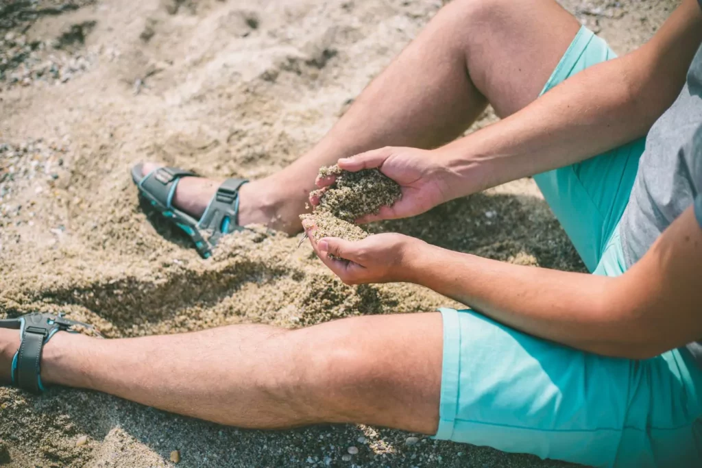 man sitting in the sand running sand through his fingers, feeling shame