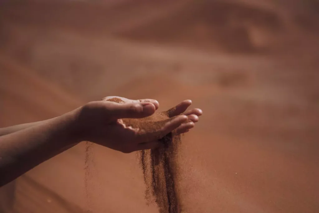 a person holding sand with it running through their fingers - holding all things loosely including your self-esteem