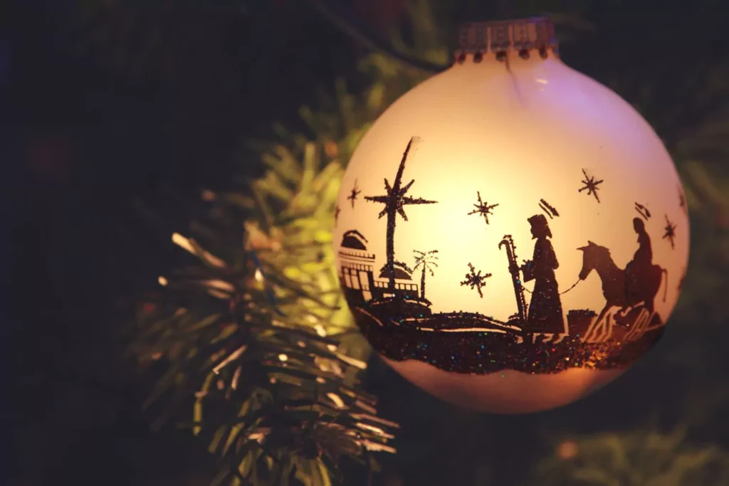 Christmas ornament with the nativity scene painted on it, hanging on a tree, illuminated. The wonder of Christmas