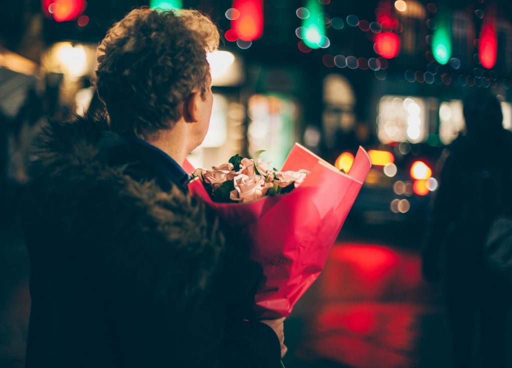 Man standing on street corner in winter with bouquet of flowers in winter