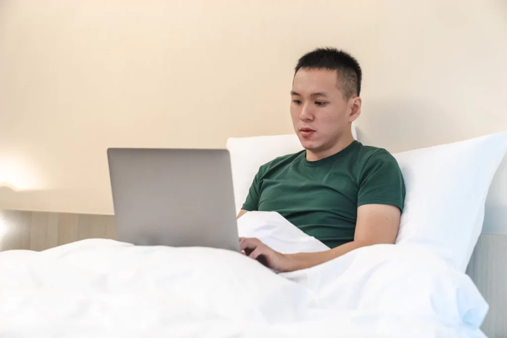 man sitting in bed looking at this laptop - is porn killing men's desire for marriage?