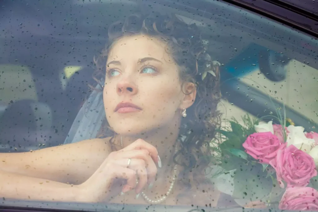 a woman hoping for marriage, looking out a rainy window dressed for a wedding