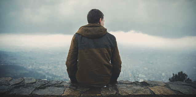 Young adult man sitting on cliff by water