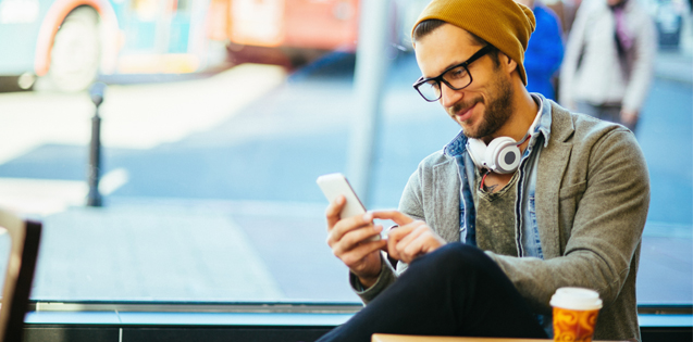 Hipster man sitting outside looking at phone