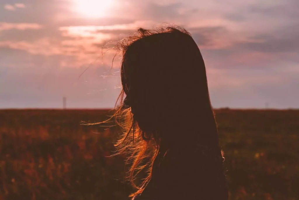 single woman with wind blowing through her hair at sunset