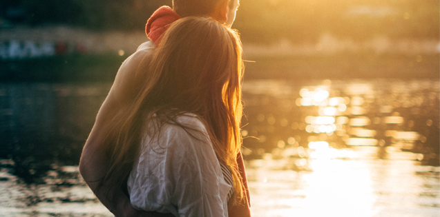 Couple standing in front of a lake at sunset.