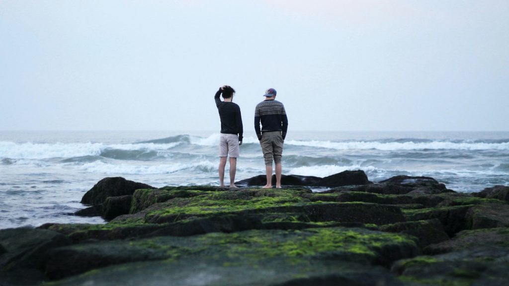 two men standing on rock by ocean