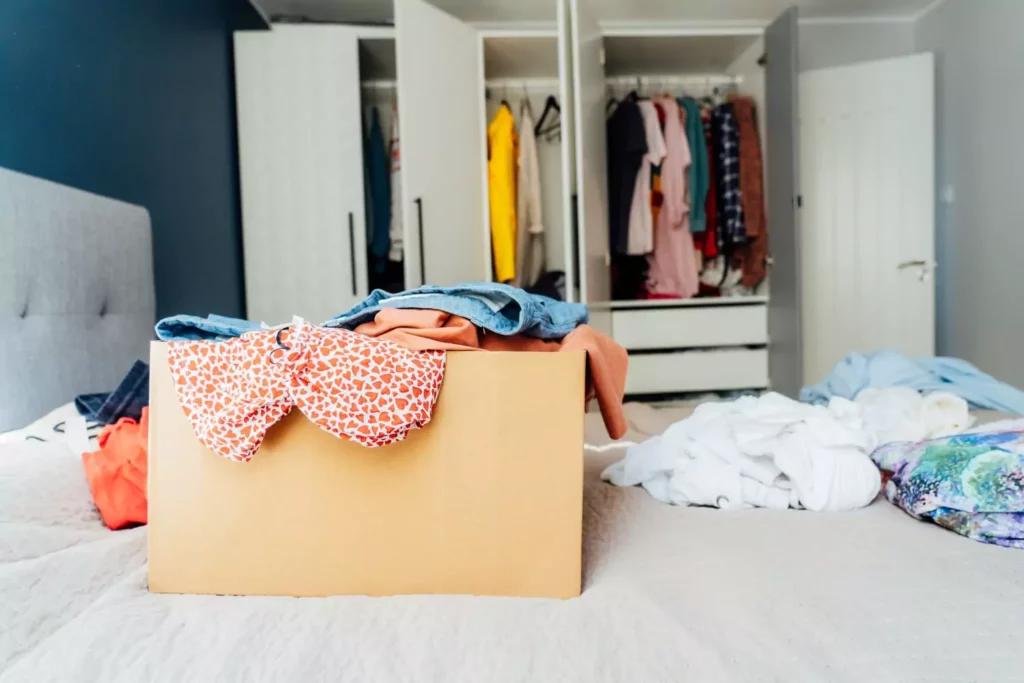 box of clothes on a bed with a closet in the background - decluttering