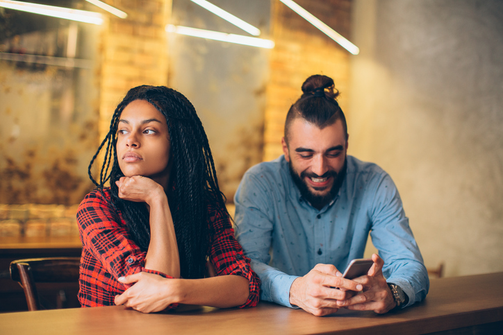 Man texting on phone while on date woman looking annoyed