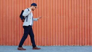 Man in casualwear carrying rucksack and texting on mobile smart phone