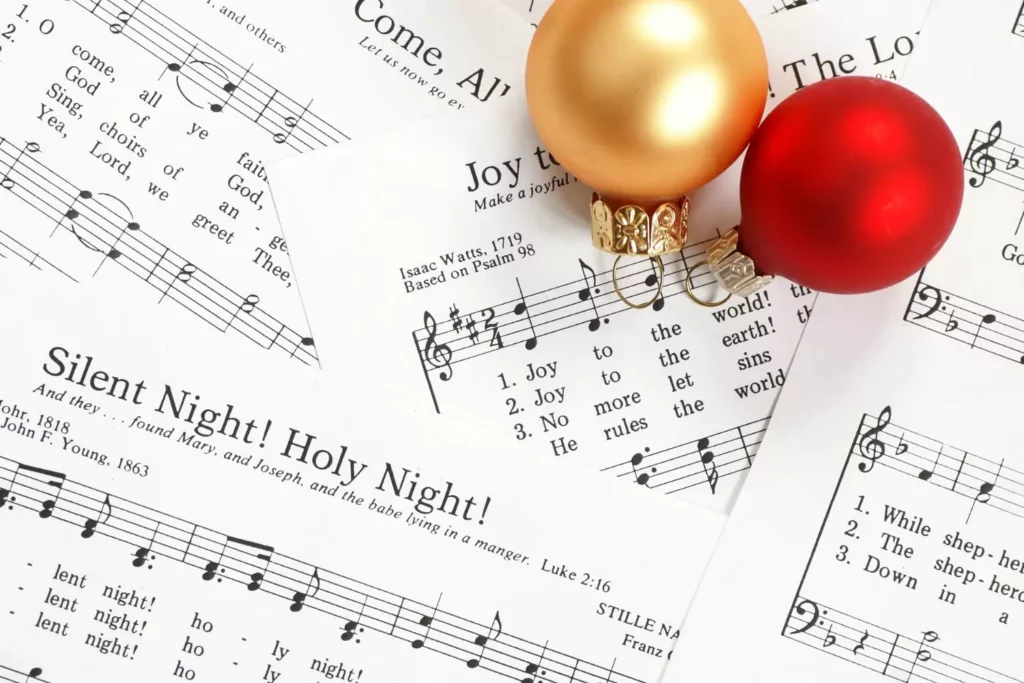 sheets of music for Christmas carols with two ornaments sitting atop the sheet music