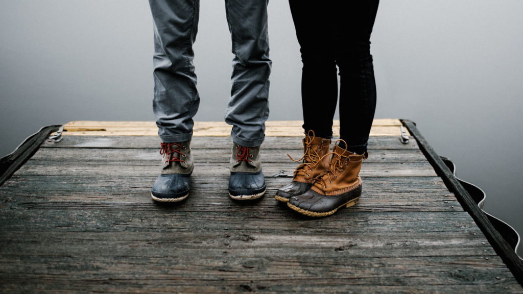 A woman and man standing on a dock, only their boots and lower legs are pictures; rainy day.