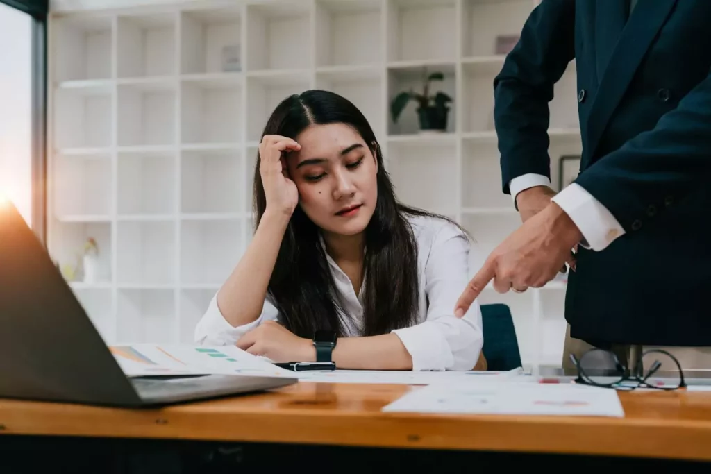 Frustrated woman working at her computer with her boss pointing at her work