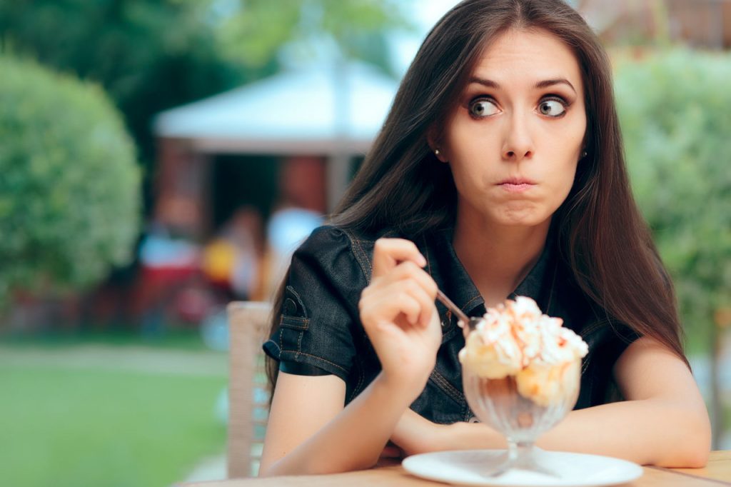 young woman feeling guilty as she eats ice cream dessert