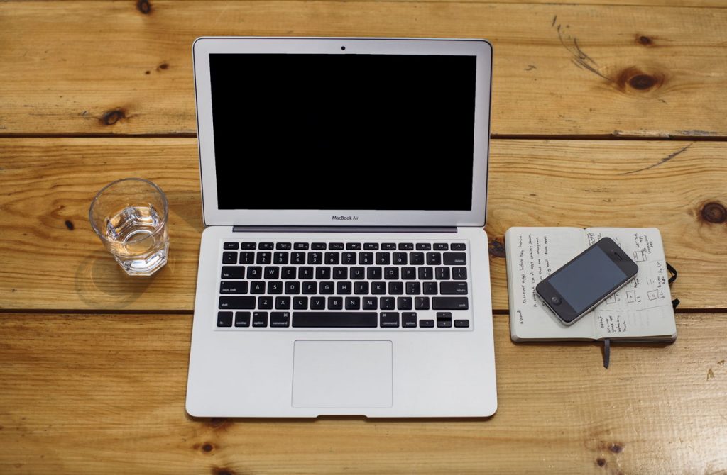 open macbook air, glass of water, notebook, and iphone