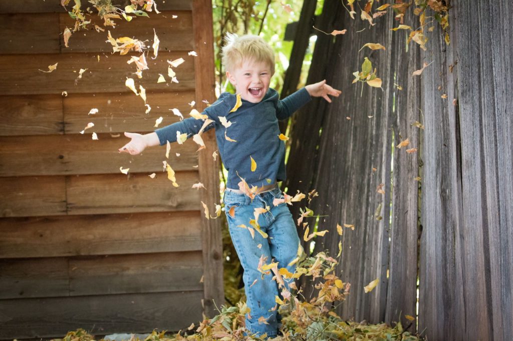 little boy playing in pile of leaves
