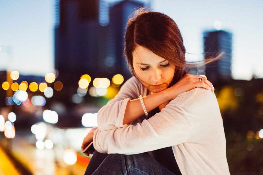 woman sitting, weary, looking down, with city behind