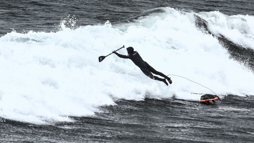 man falling off board into huge wave