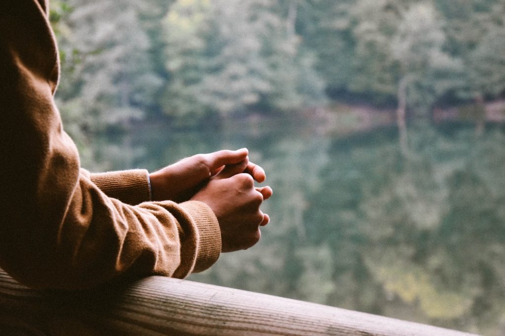 person who's holding hands (praying/thinking), looking off a balcony in the mountains