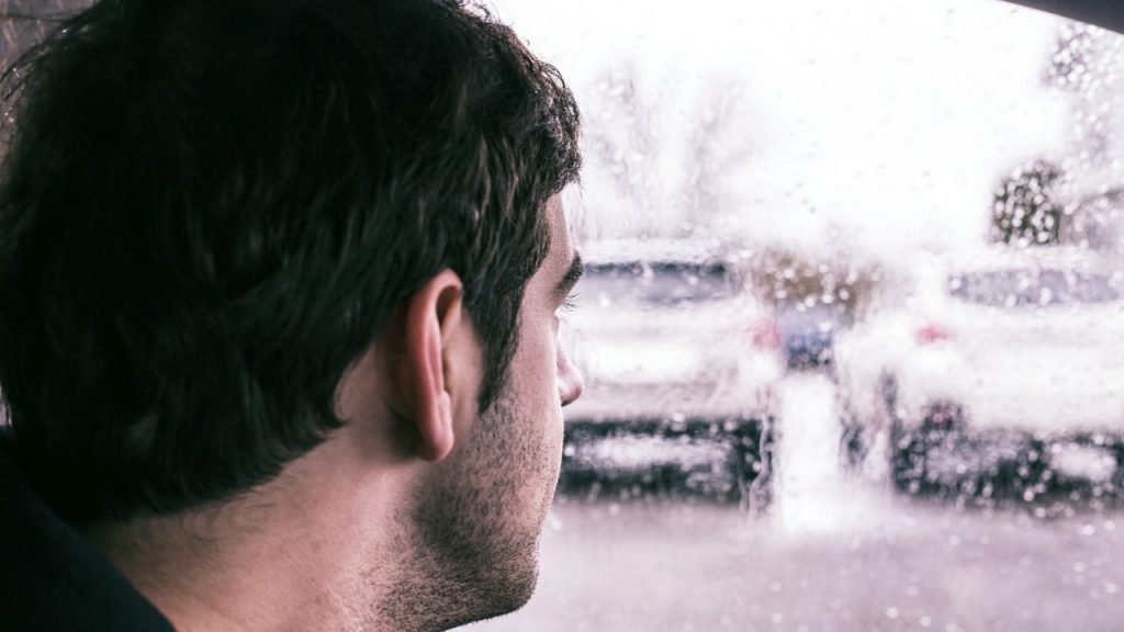 man looking out car window at rain