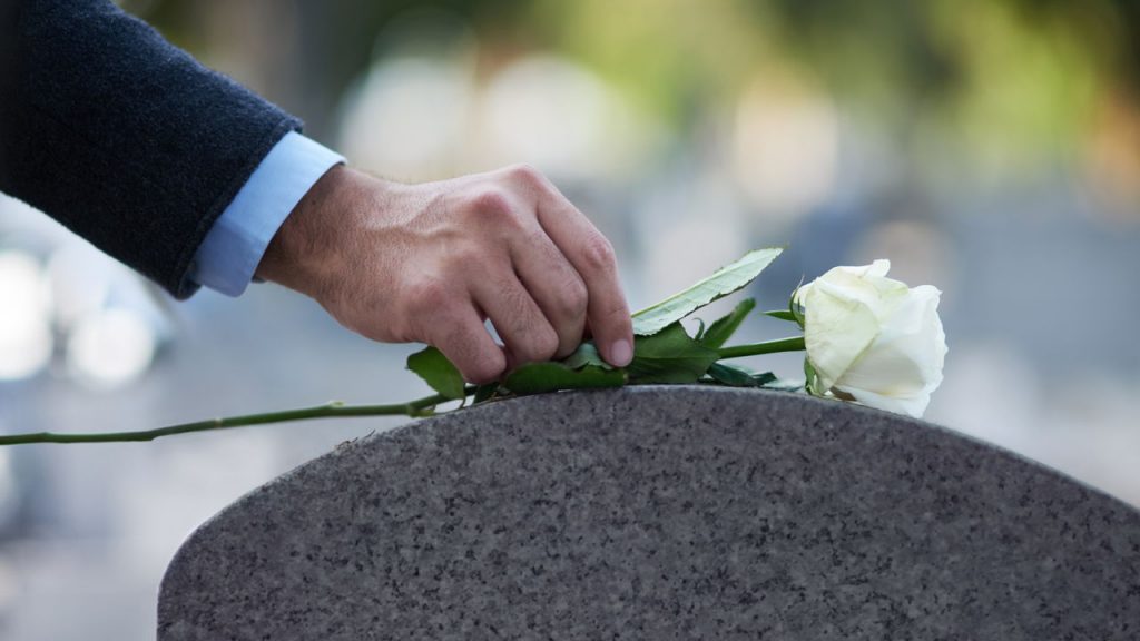 man placing rose on gravestone