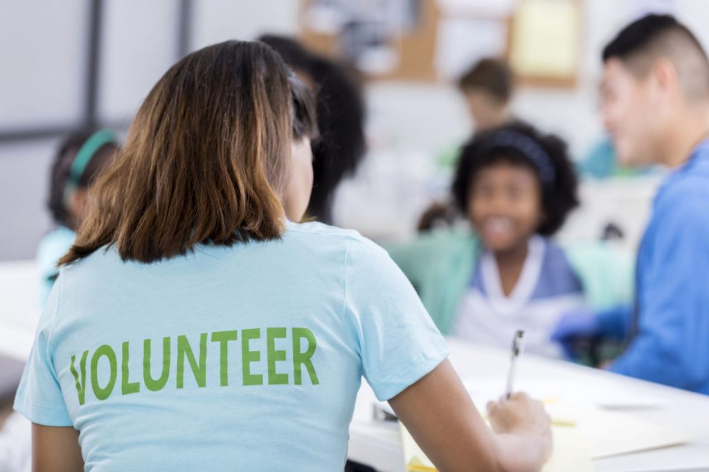 woman wearing a "Volunteer" t-shirt is helping kids and their parents