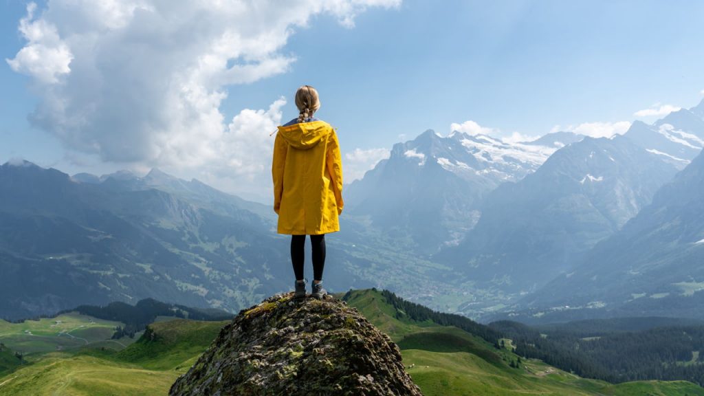 woman in yellow raincoat standing on a mountaintop, looking at the horizon