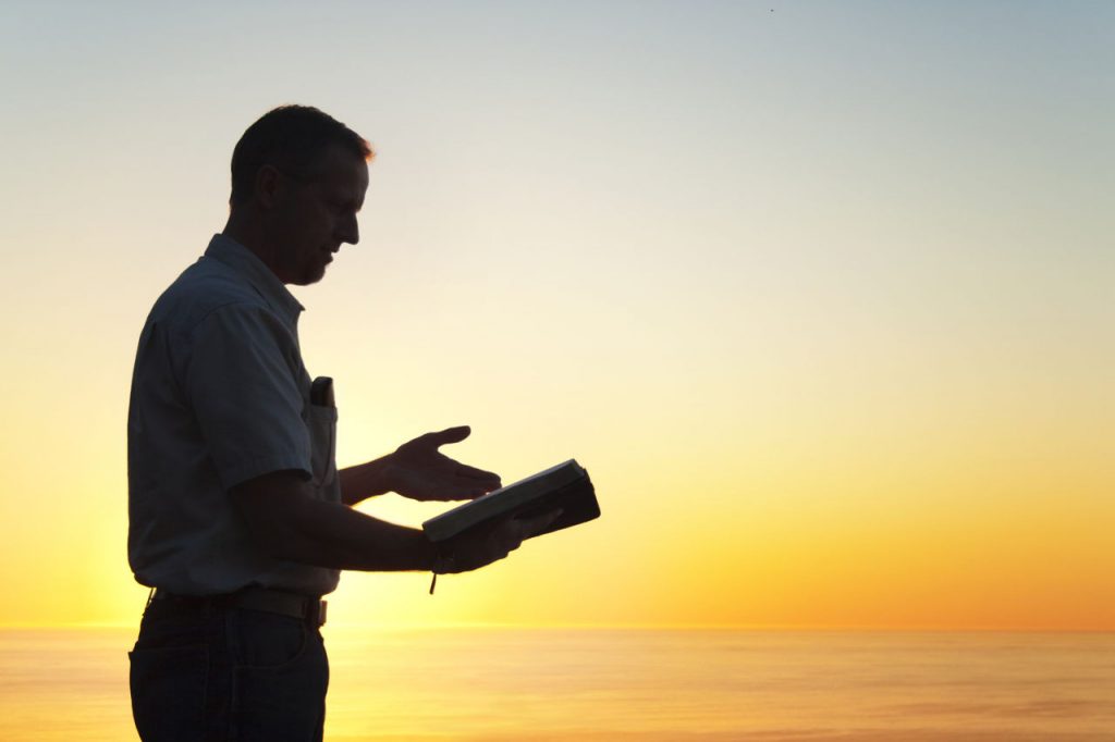 man holding bible, preaching, with a sunset background