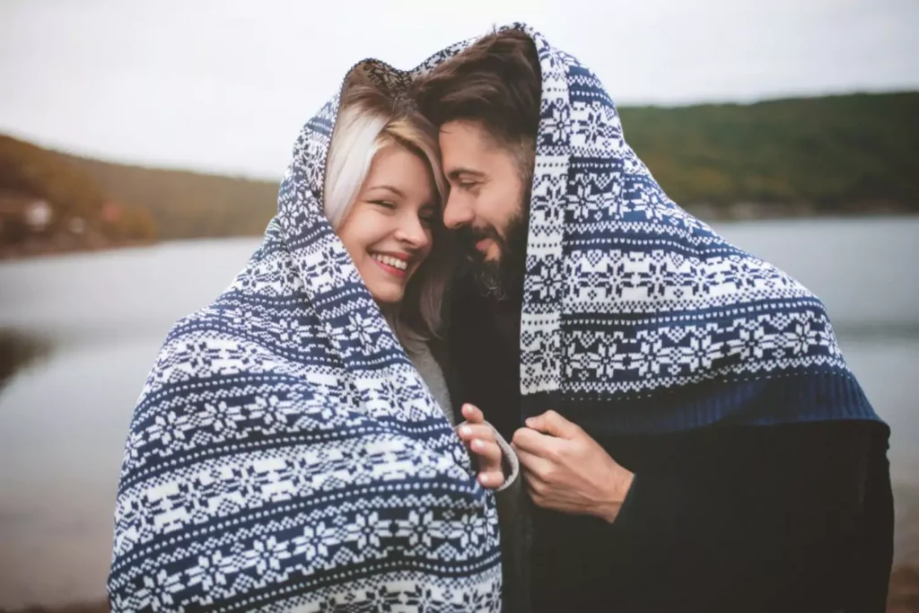 a woman and man snuggling under a blanket; they just got engaged