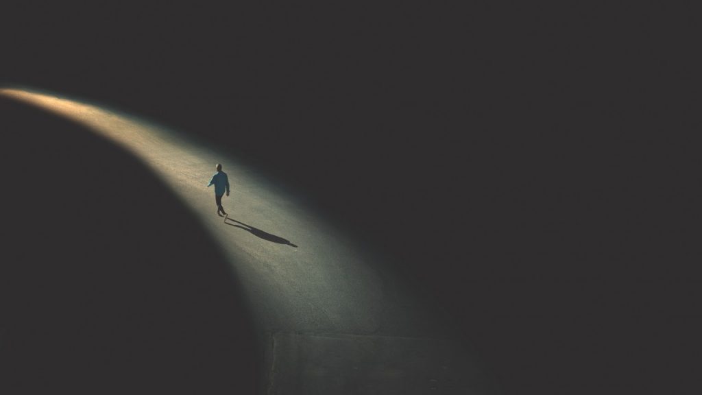 person walking on path of light in darkness