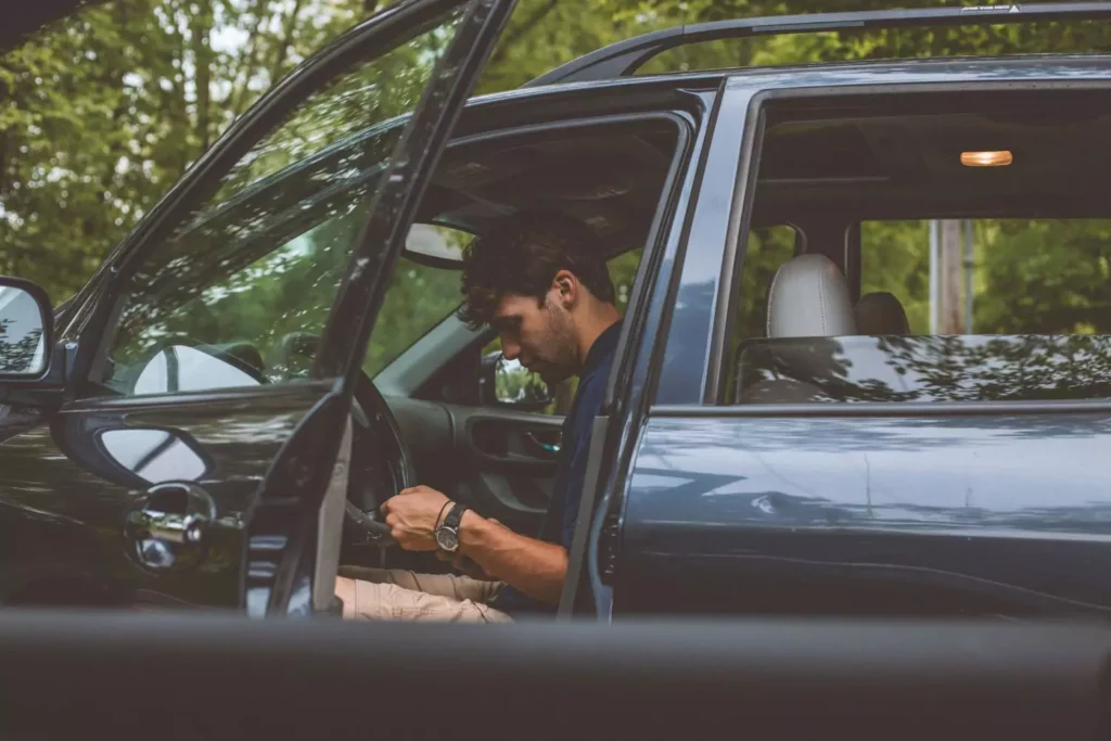 Man sitting in his car with the door open texting his friend "on my way" because he is running late