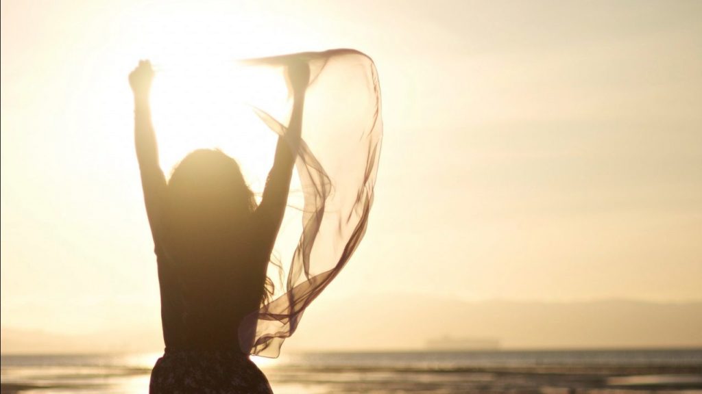 silhouette of woman at beach with arms up